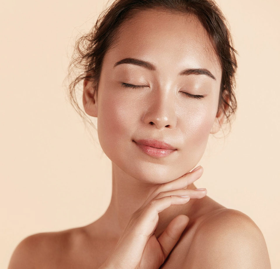 Beautiful asian girl model touching fresh glowing hydrated facial skin on beige background closeup