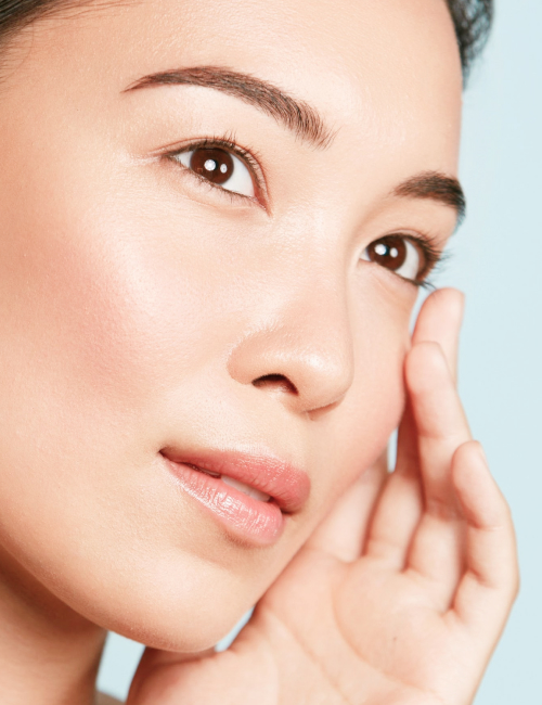 Beautiful Asian girl model with natural makeup touching glowing hydrated skin Portuguese face