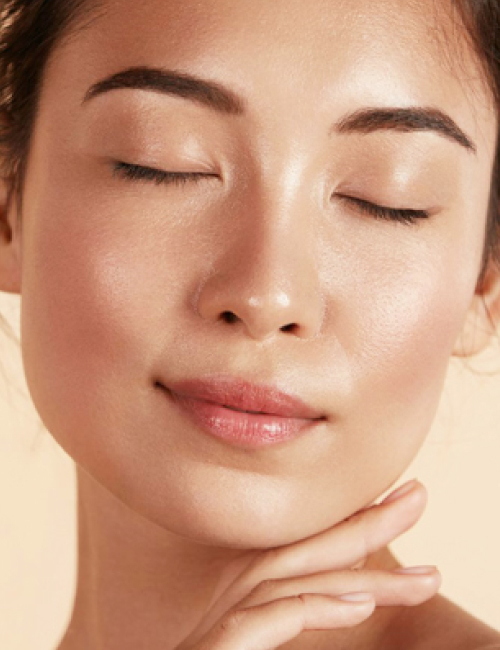 Beautiful asian girl model touching fresh glowing hydrated facial skin on beige background closeup non-surgical